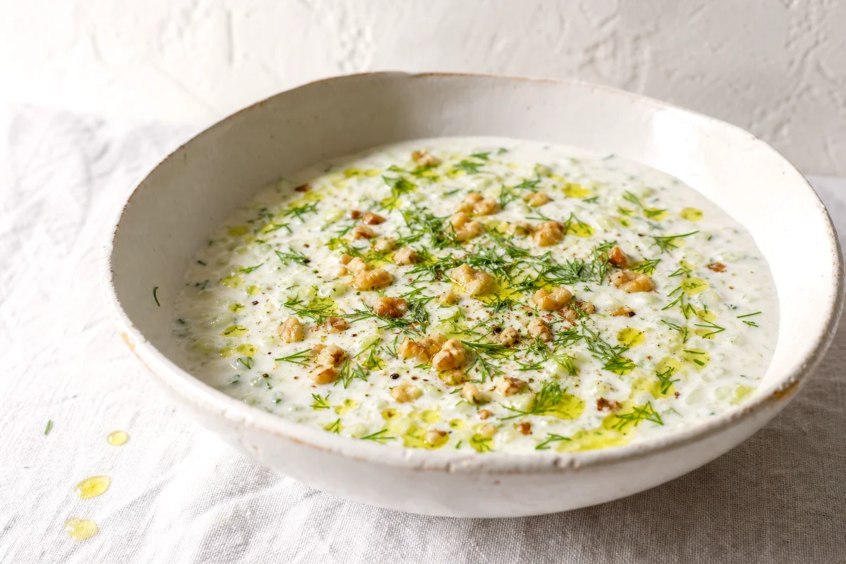 Cold cucumber yogurt soup topped with dill, walnuts, olive oil, and black pepper in a white ceramic bowl