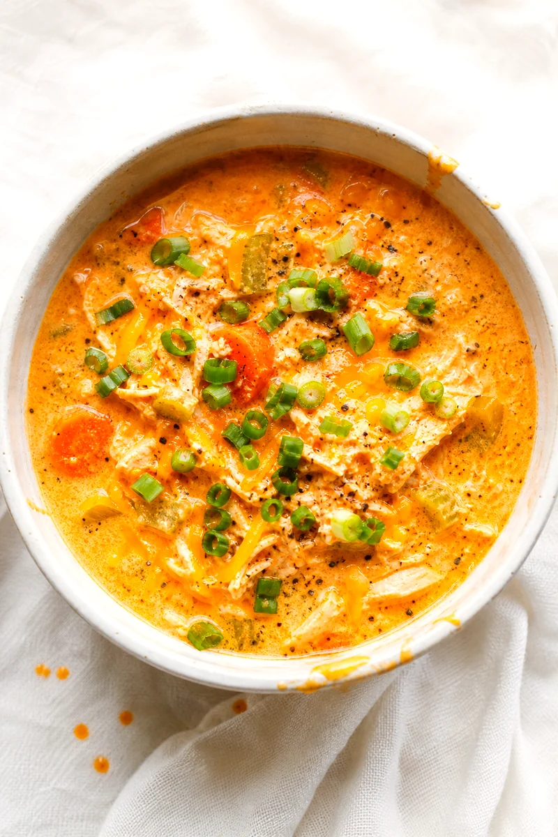 Top down view of creamy buffalo chicken soup topped with cheddar, black pepper, and sliced green onions