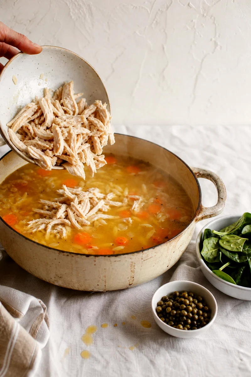 Shredded chicken going into simmering lemon broth with carrots and orzo