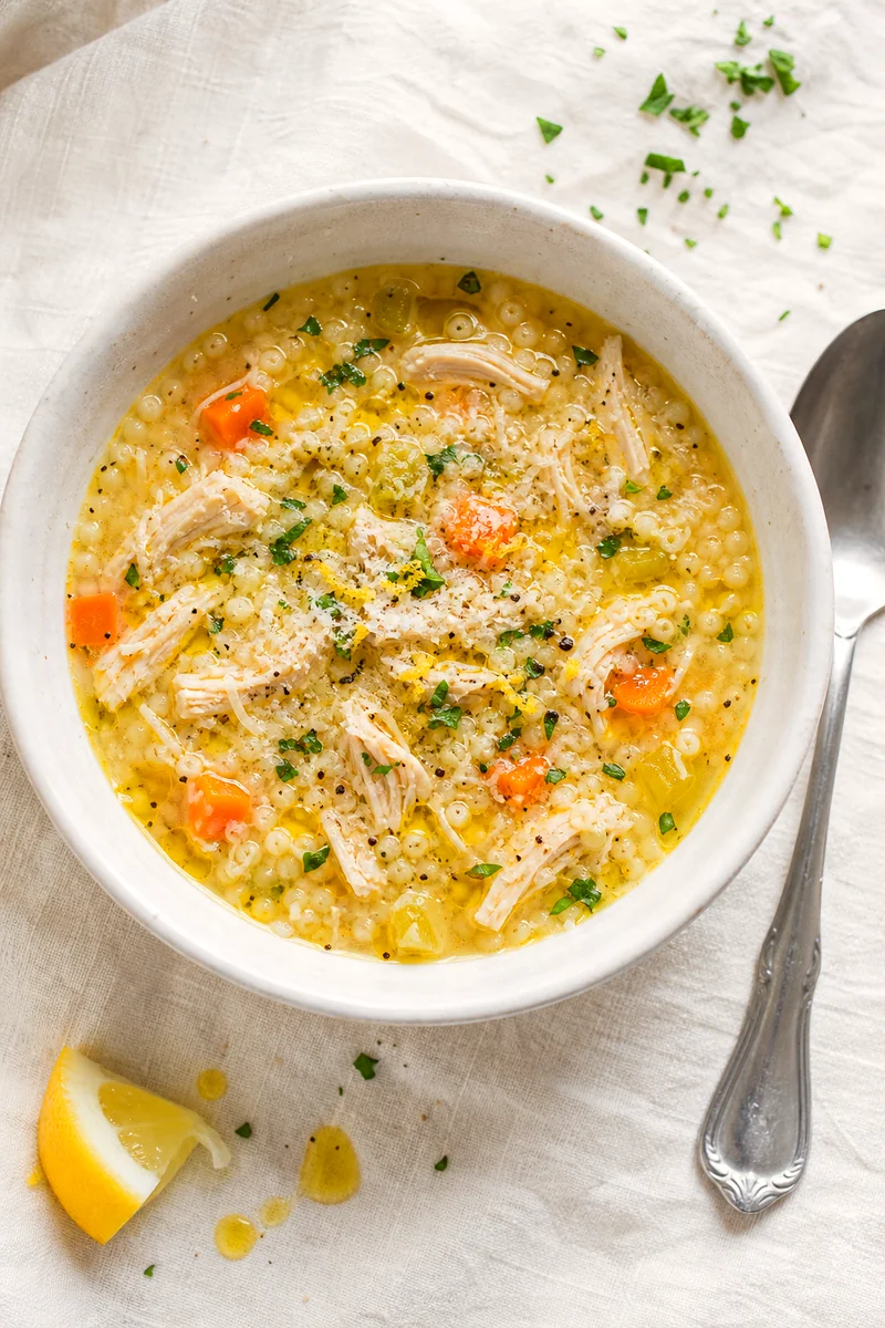 Top down bowl of golden chicken pastina soup finished with parsley, Parmesan, lemon zest, and olive oil
