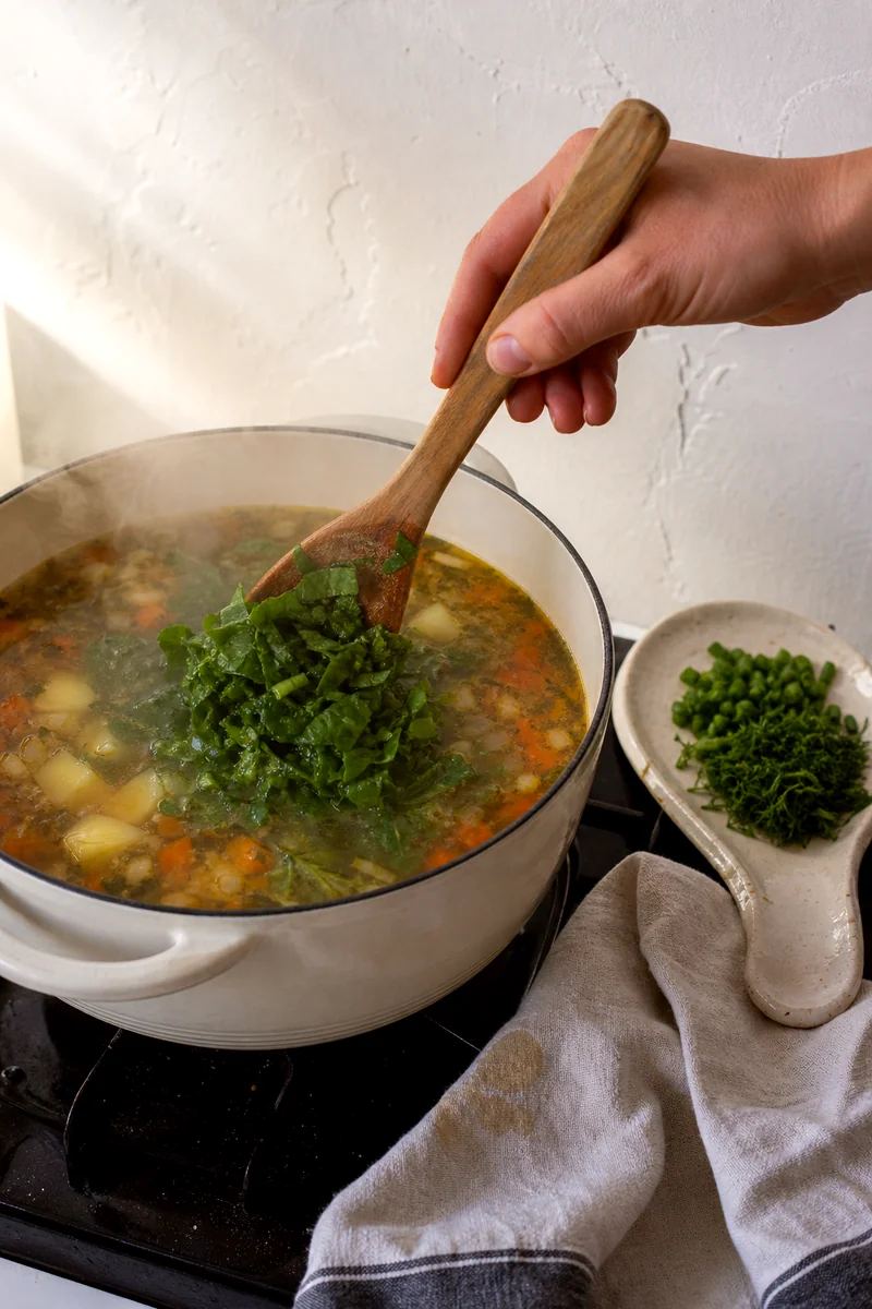 Chopped sorrel being stirred into hot broth with potatoes and carrots