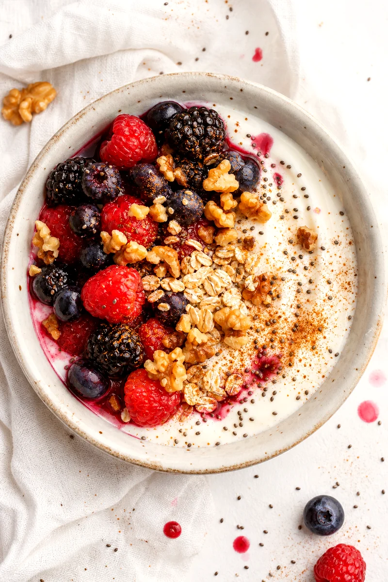 Top view of a Greek yogurt breakfast bowl with berries, oats, walnuts, chia, and cinnamon
