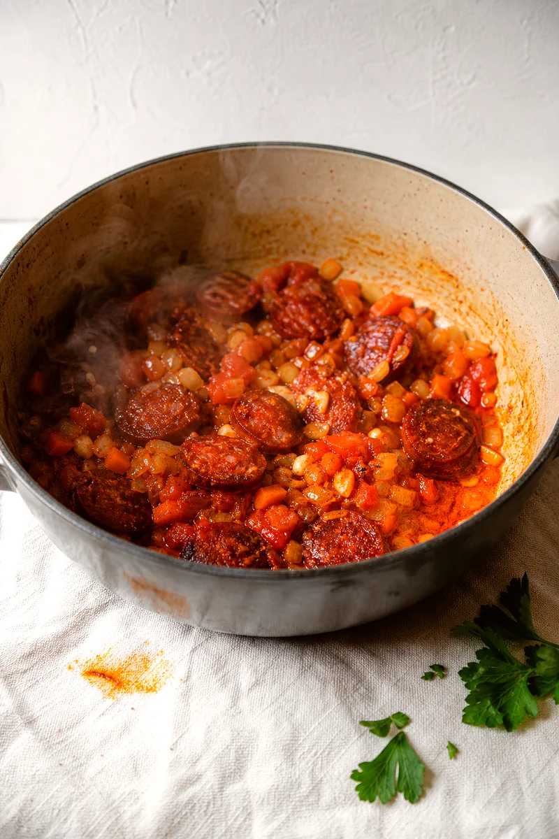 Chorizo, onion, carrots, garlic, tomatoes, and paprika cooking in a rustic pot