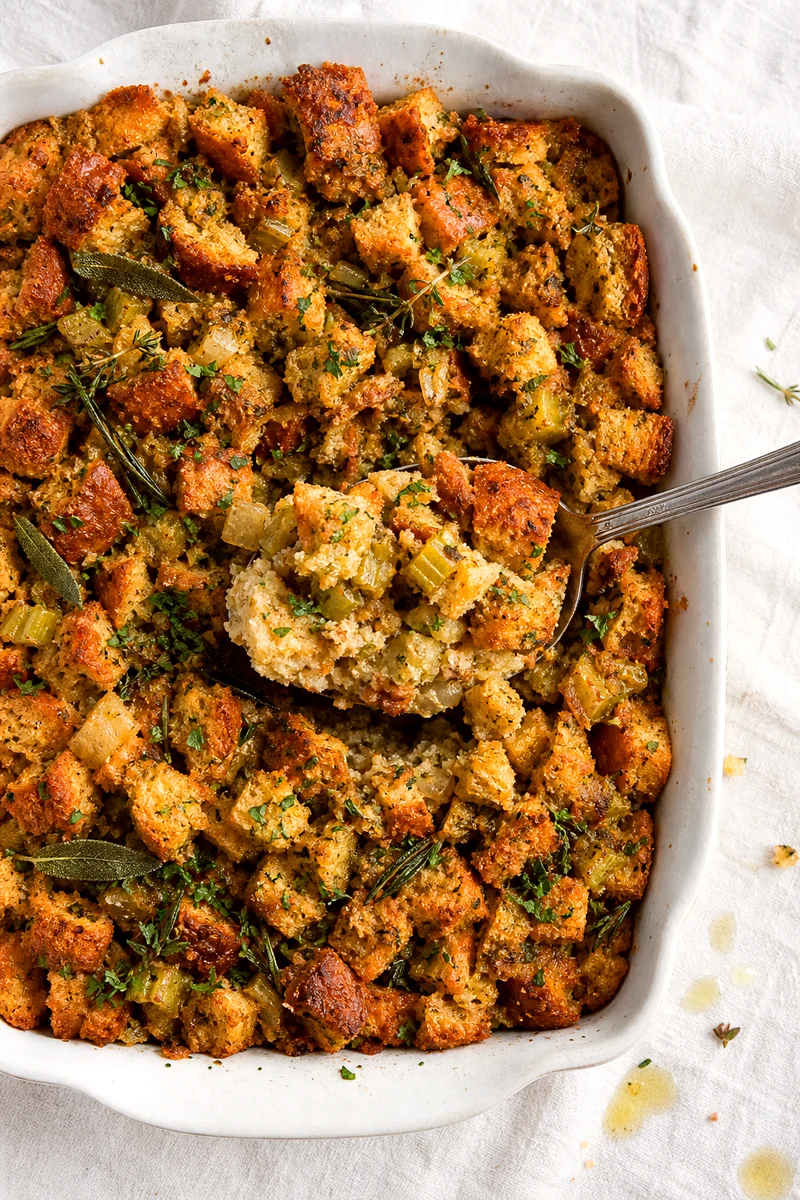 Crisp topped stuffing casserole in a white baking dish with a spoon lifting a serving