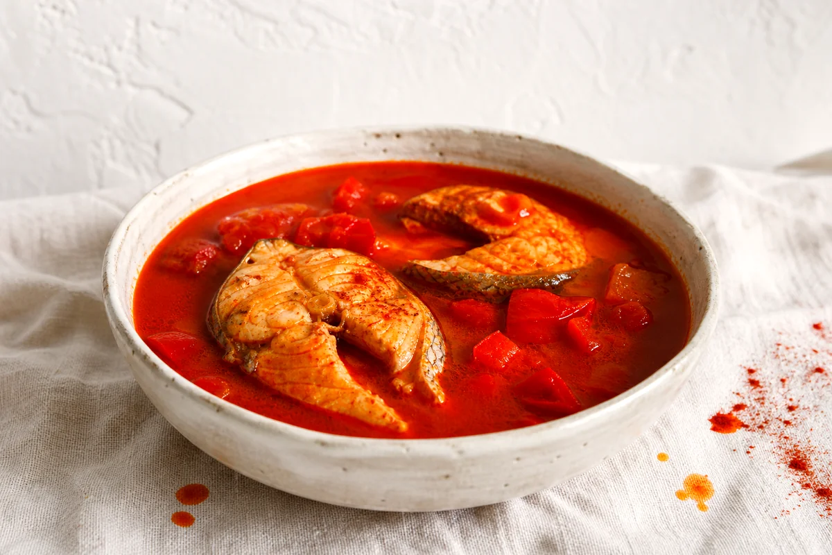 Red paprika fish soup with tender fish steaks in a white ceramic bowl