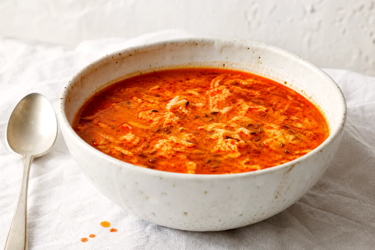 Steaming Hungarian paprika egg soup with egg ribbons in a white ceramic bowl on white linen