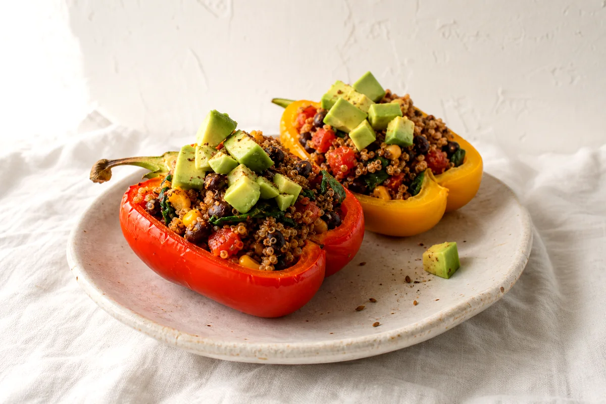 Tender stuffed bell peppers filled with quinoa, black beans, corn, tomatoes, spinach, and diced avocado
