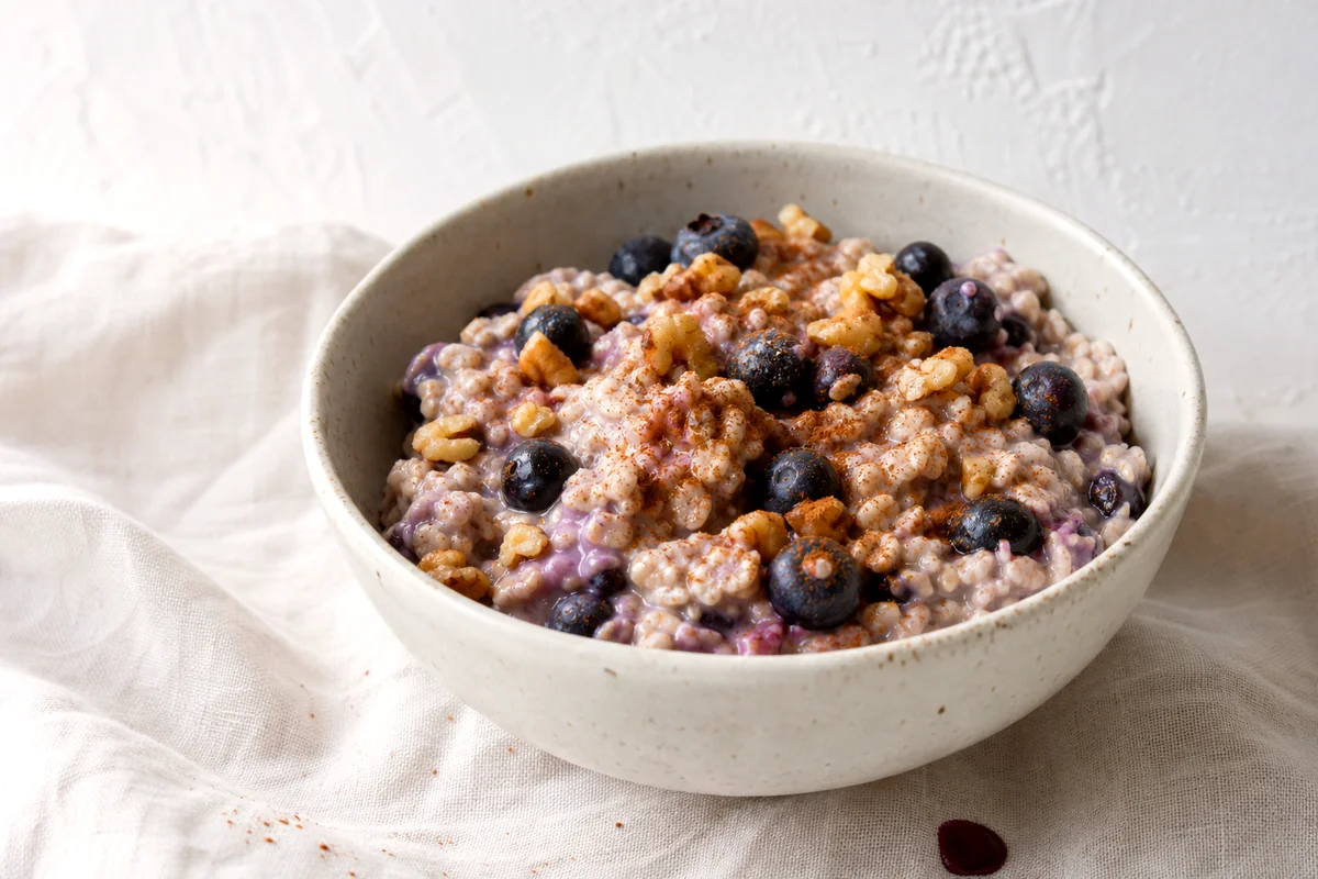 Creamy overnight oats topped with blueberries, chopped walnuts, and cinnamon in a white ceramic bowl