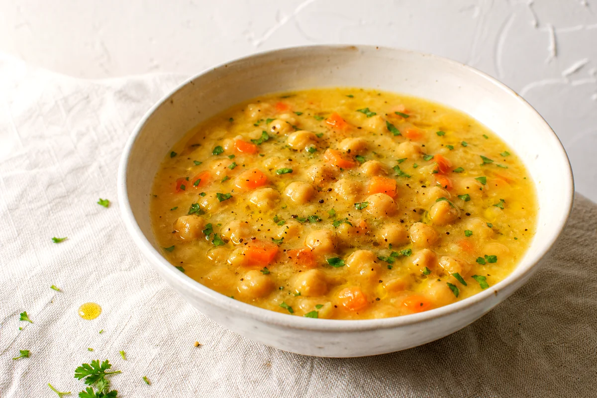 Golden chickpea lemon soup with carrots, parsley, and olive oil in a white ceramic bowl