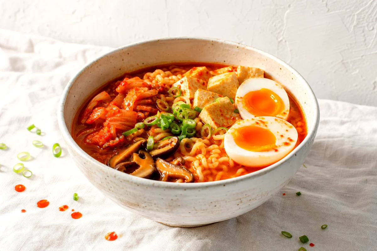 Bowl of kimchi ramen soup with noodles, tofu, mushrooms, green onions, and a soft boiled egg