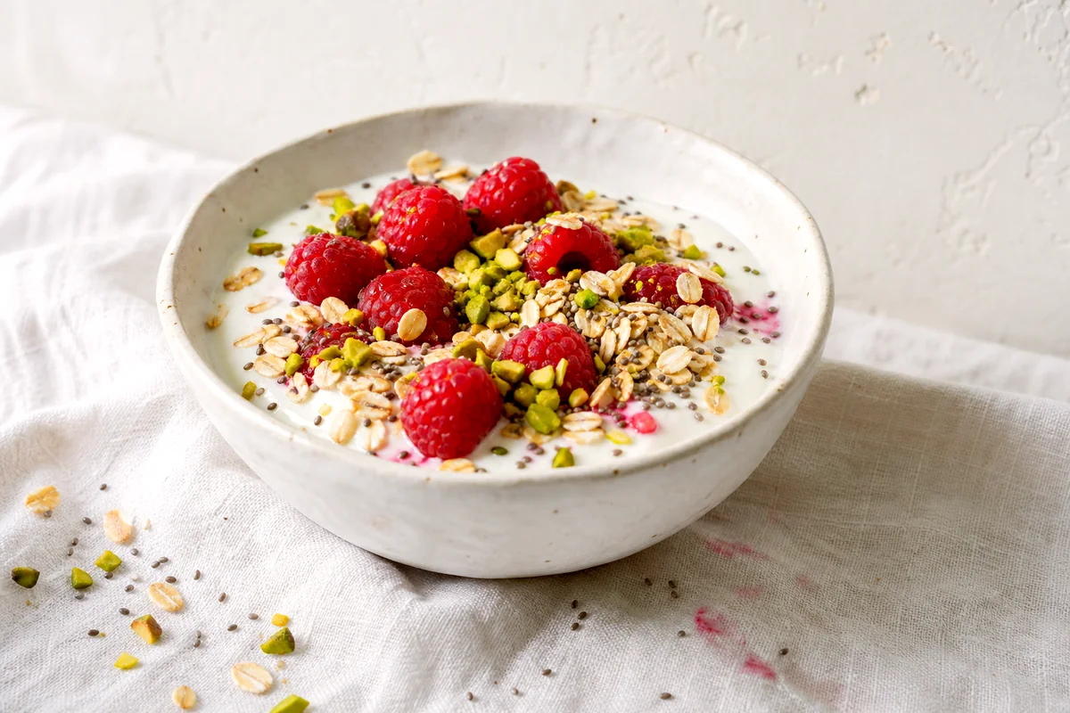Creamy Greek yogurt topped with raspberries, pistachios, oats, and chia seeds in a white ceramic bowl