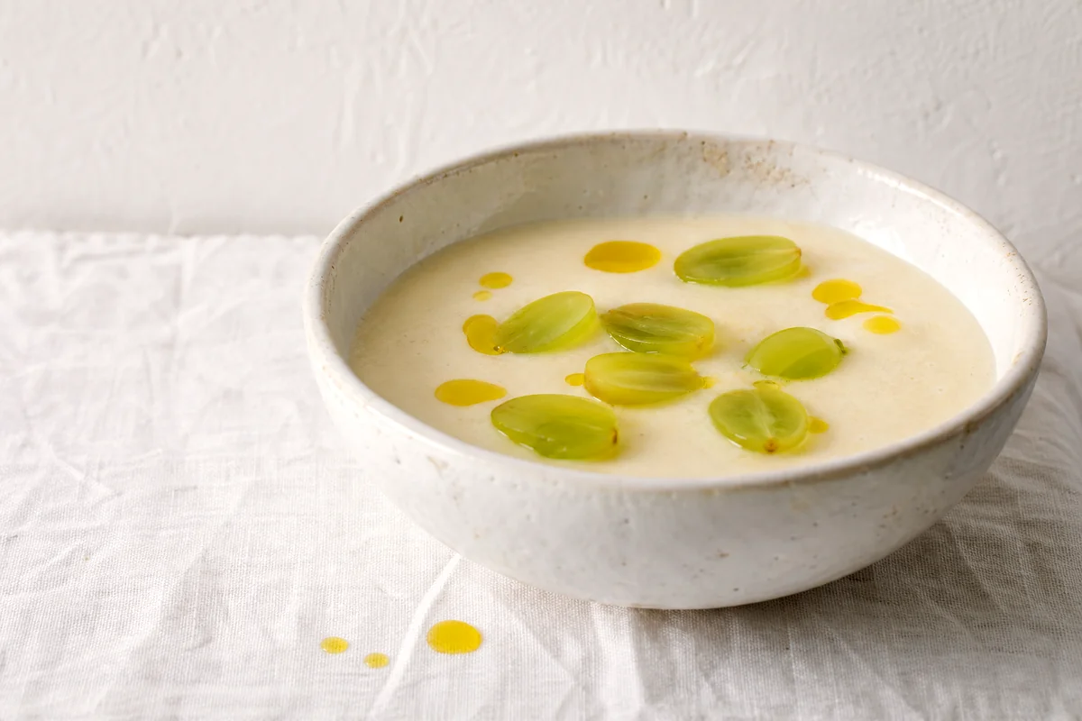 Silky almond garlic soup topped with halved green grapes in a white ceramic bowl