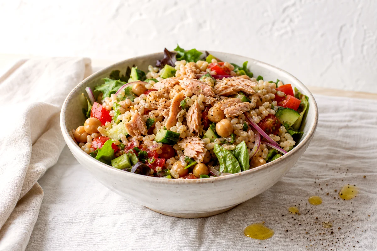 Lemony tuna, chickpea, brown rice, cucumber, tomato, greens, and red onion salad in a white ceramic bowl